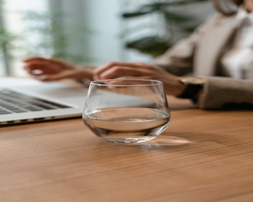 Glass of water on an office desk next to a laptop
